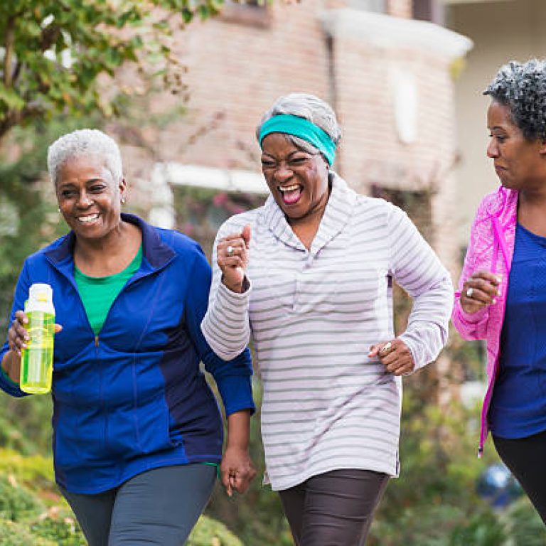 A group of three senior African America women exercising together, jogging or power walking along a sidewalk in a residential neighborhood.  They are having fun, laughing.
